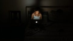 seorang wanita menyalakan laptop di kamar yang gelap