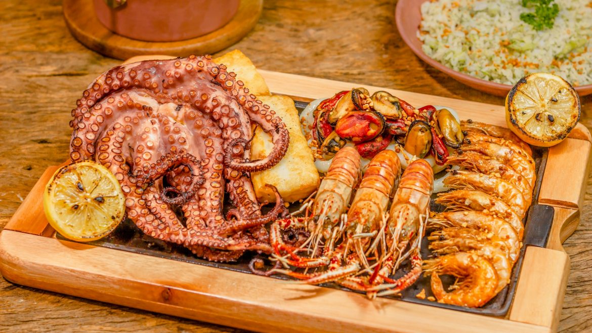 berbagai jenis seafood seperti gurita, udang, kerang di atas nampan kayu di atas meja