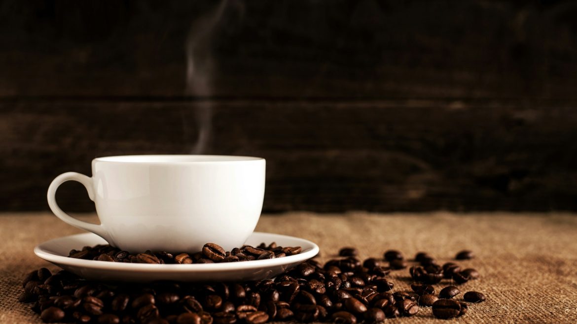 cangkir keramik putih dengan biji kopi di atas kain coklat bertekstur
