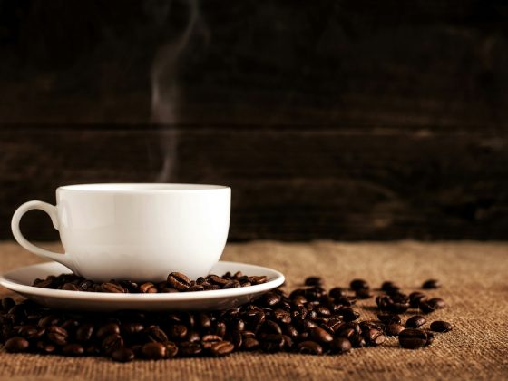 cangkir keramik putih dengan biji kopi di atas kain coklat bertekstur
