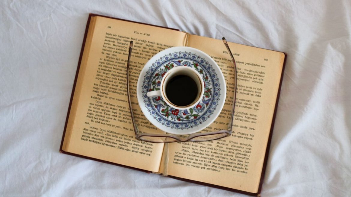 secangkir kopi dan kacamata di atas buku, di atas kasur
