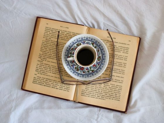 secangkir kopi dan kacamata di atas buku, di atas kasur