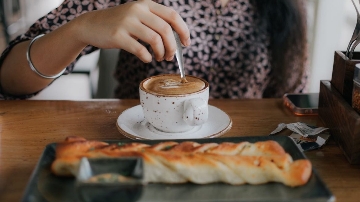 perempuan sedang minum kopi dan roti di cafe