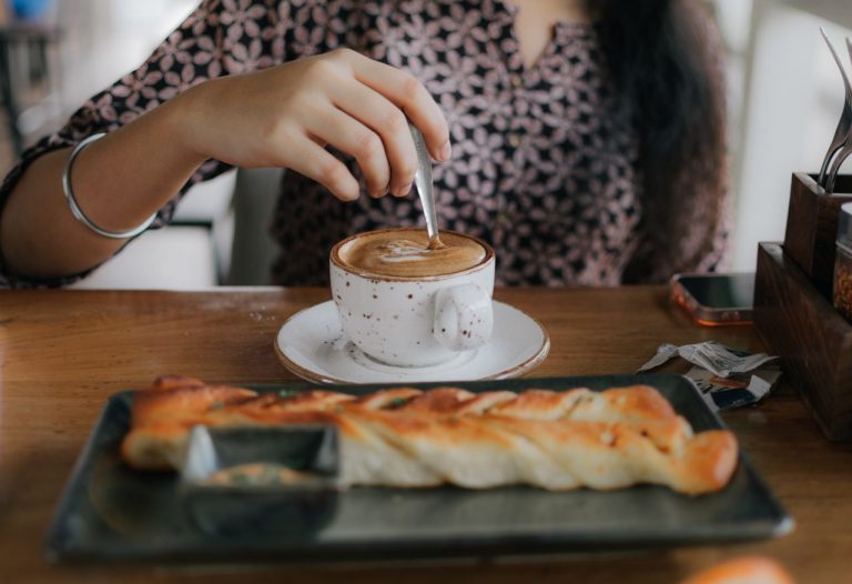 perempuan sedang minum kopi dan roti di cafe