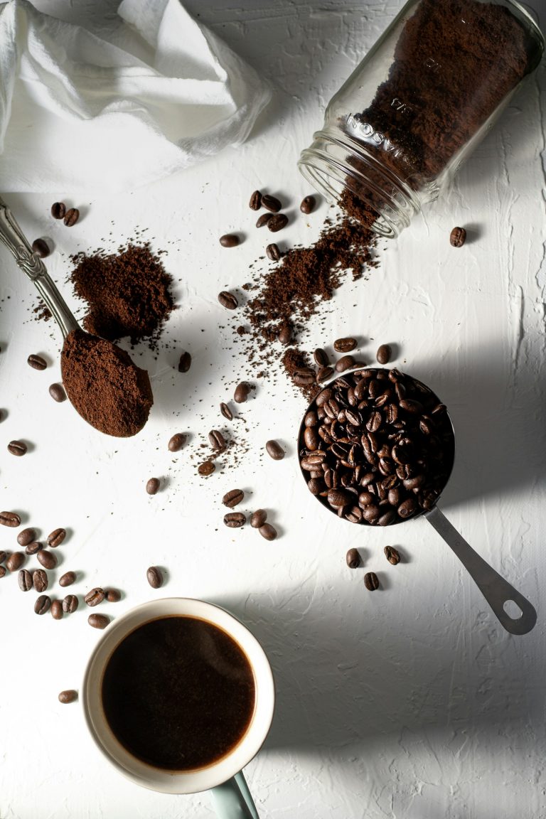 secangkir kopi, sesendok kopi bubuk, sewadah bijih kopi, botol kaca berisi kopi bubuk jatuh di atas meja, high angle shoot