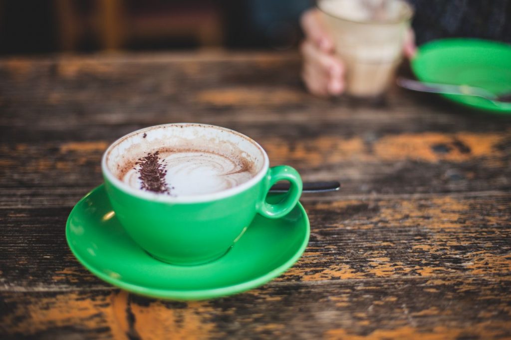 cangkir keramik hijau dengan cappucino di atas meja