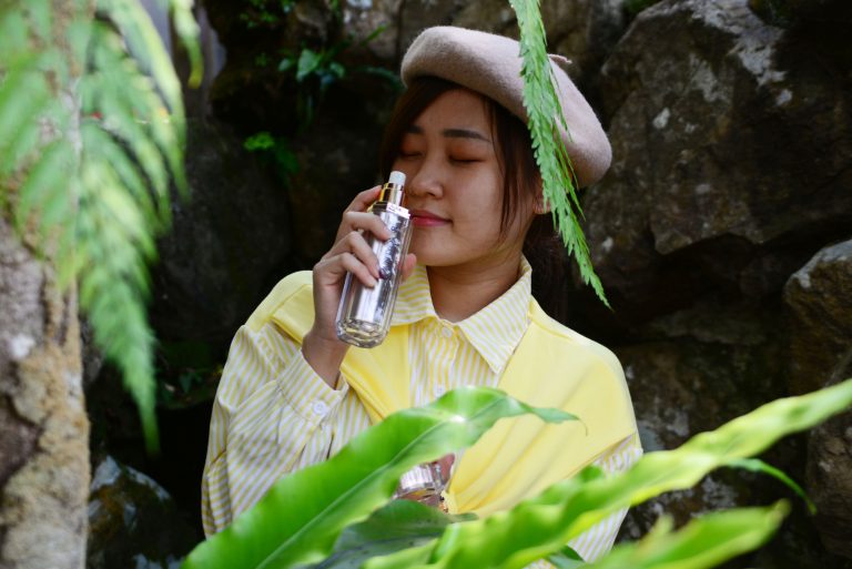 perempuan sedang mengendus wangi dari botol parfum